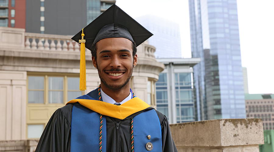 A Suffolk student wearing his cap and gown in Boston to prepare for commencement.