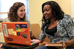 Two students smiling and looking at a laptop computer